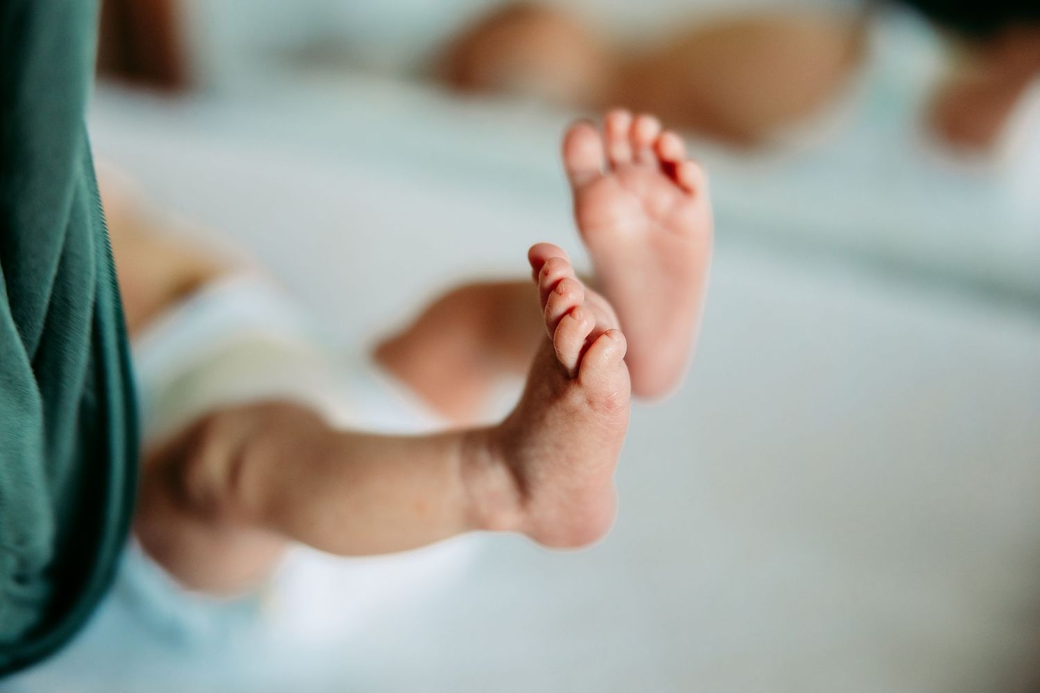 Close-up photo of tiny newborn baby feet against a soft teal-colored background.