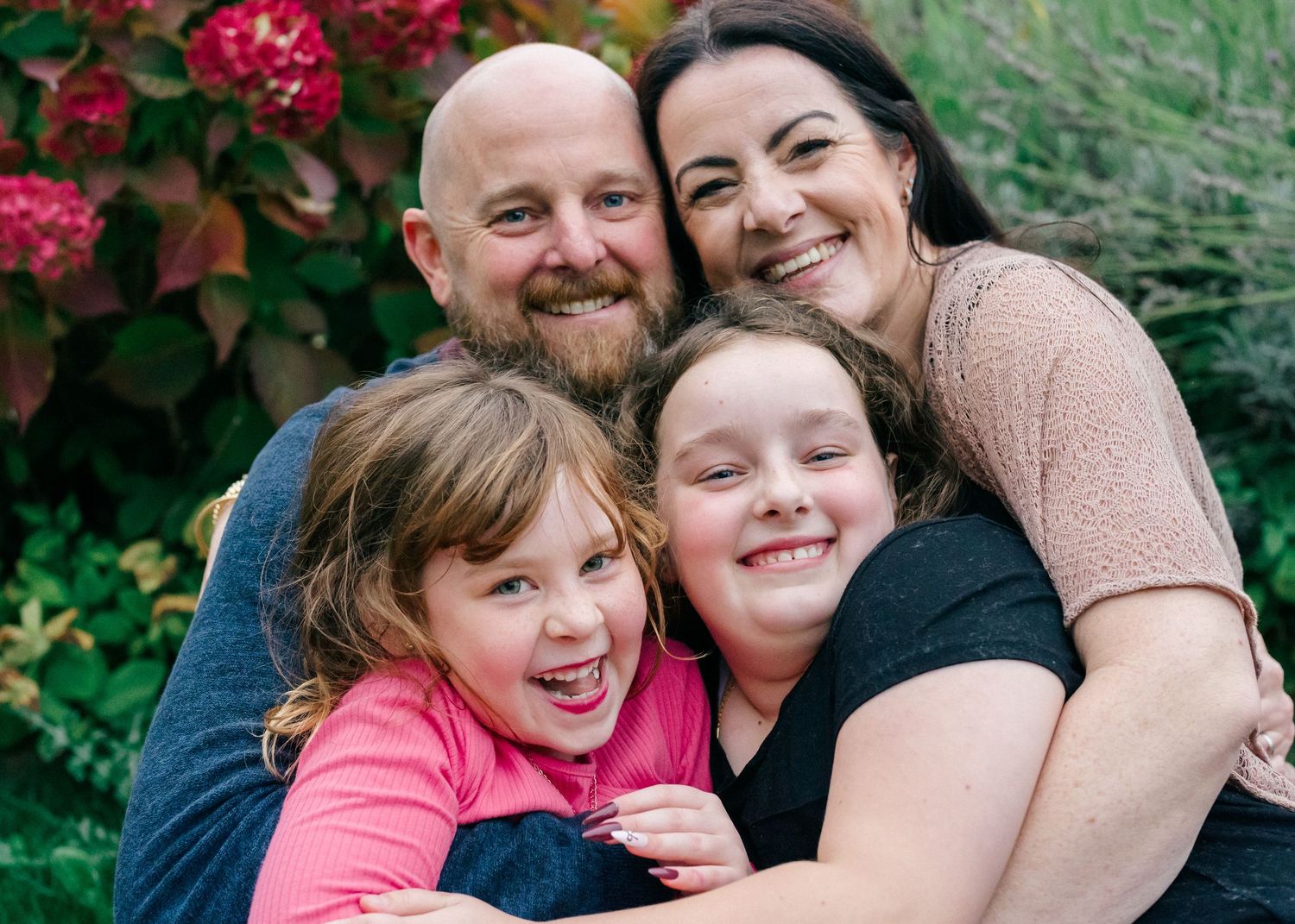 Documentary family photography in Gloucestershire showing parents and children hugging together outdoors during a relaxed family session