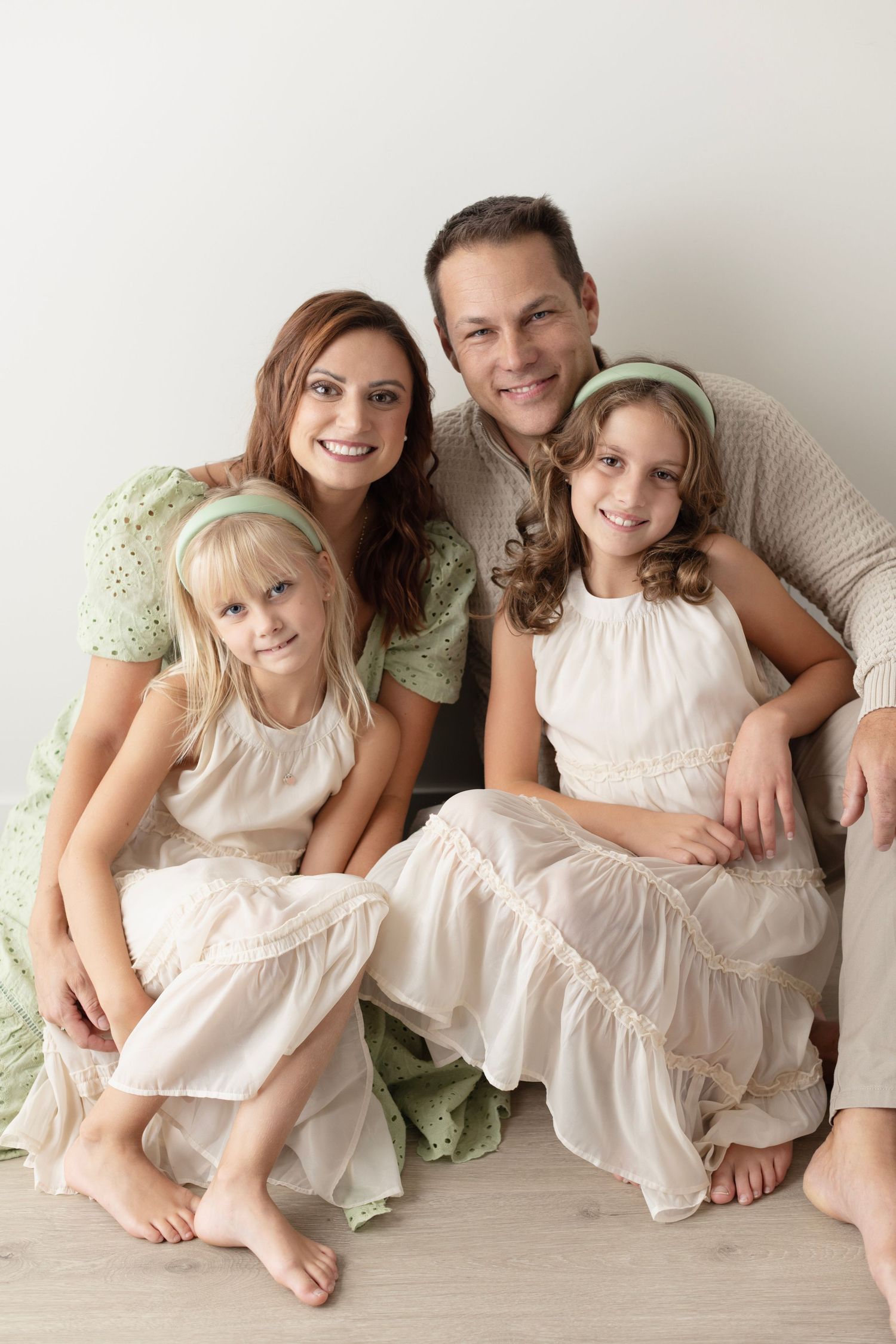 A series of intimate family portraits showing people in white dresses and casual clothing lying together on a light backdrop.