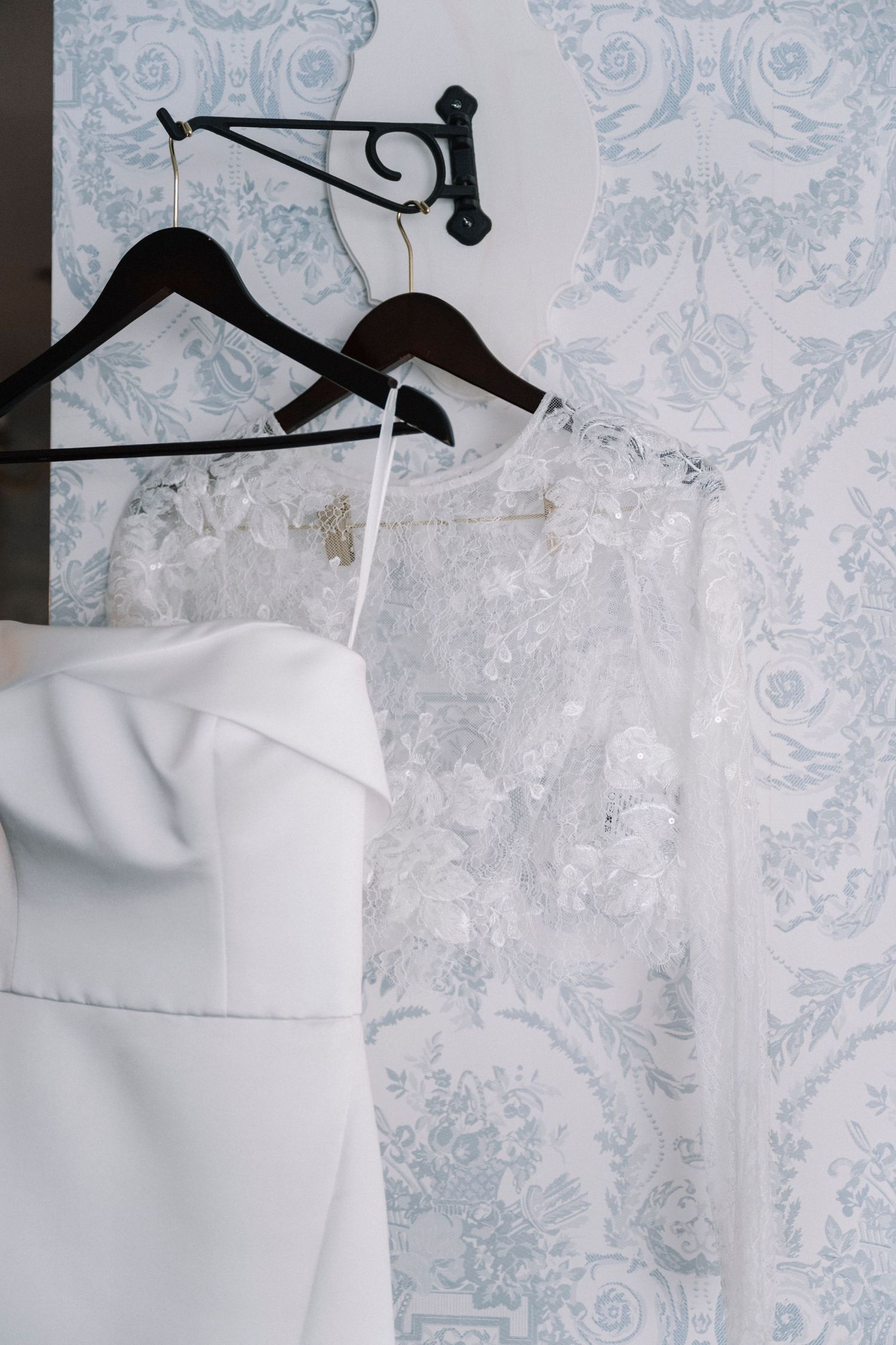 White garments hanging on black hangers against a delicate blue and white floral wallpaper background.
