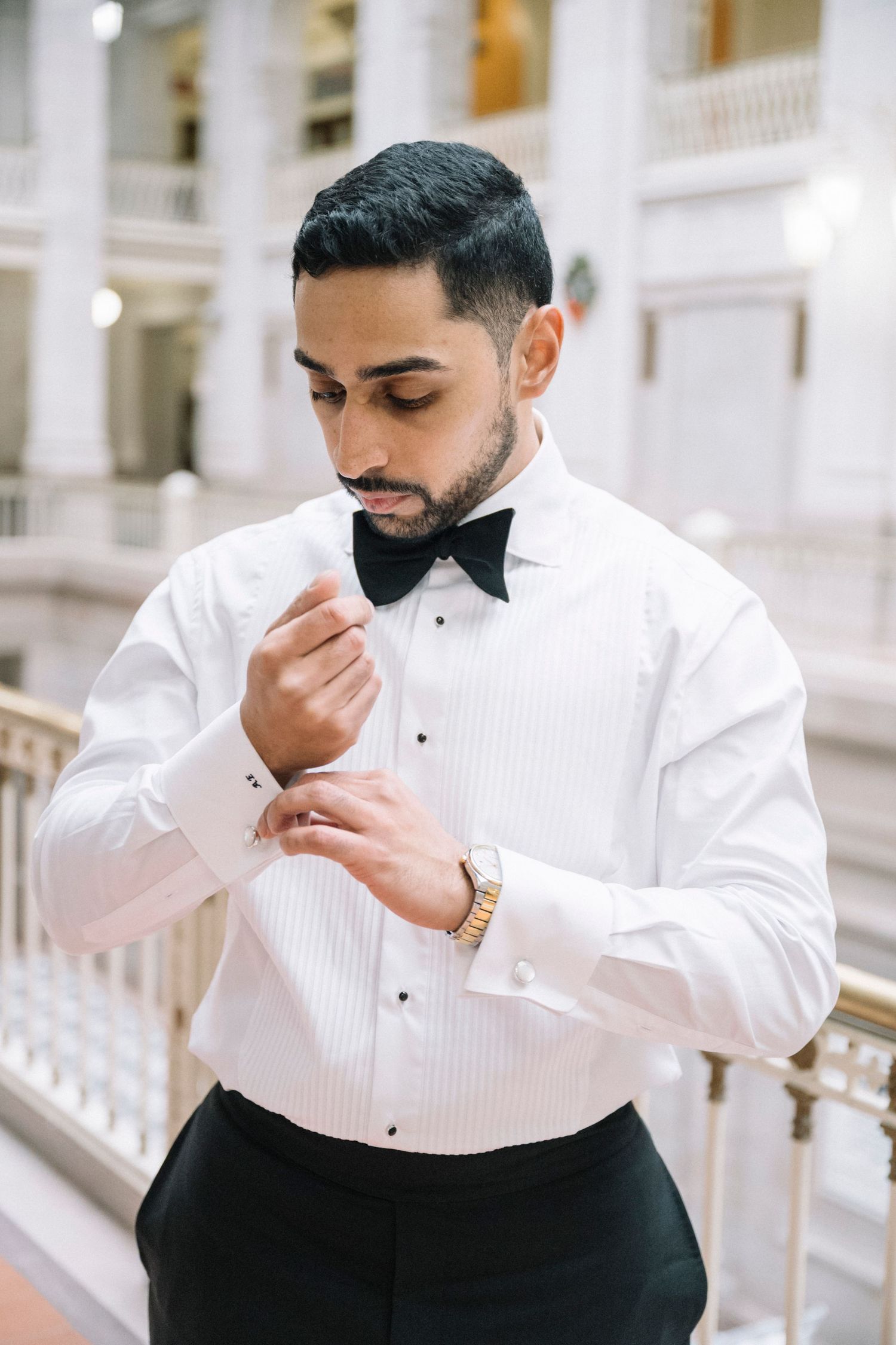 Person in formal white tuxedo shirt and black bow tie adjusting their collar.