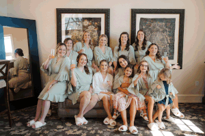 A group in matching light blue robes and white sneakers poses together on a couch in a sunlit room.