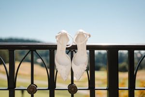 White ballet shoes hang from black metal railing against a blurred outdoor background at sunset.