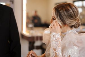 A bride in an elegant lace wedding dress gets ready for her special day with the help of attendants.