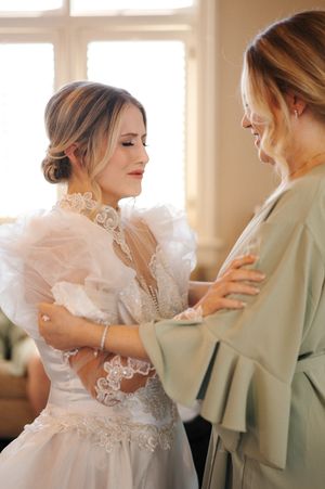Two people share an emotional embrace during a wedding, with one wearing an elegant white gown with lace details.