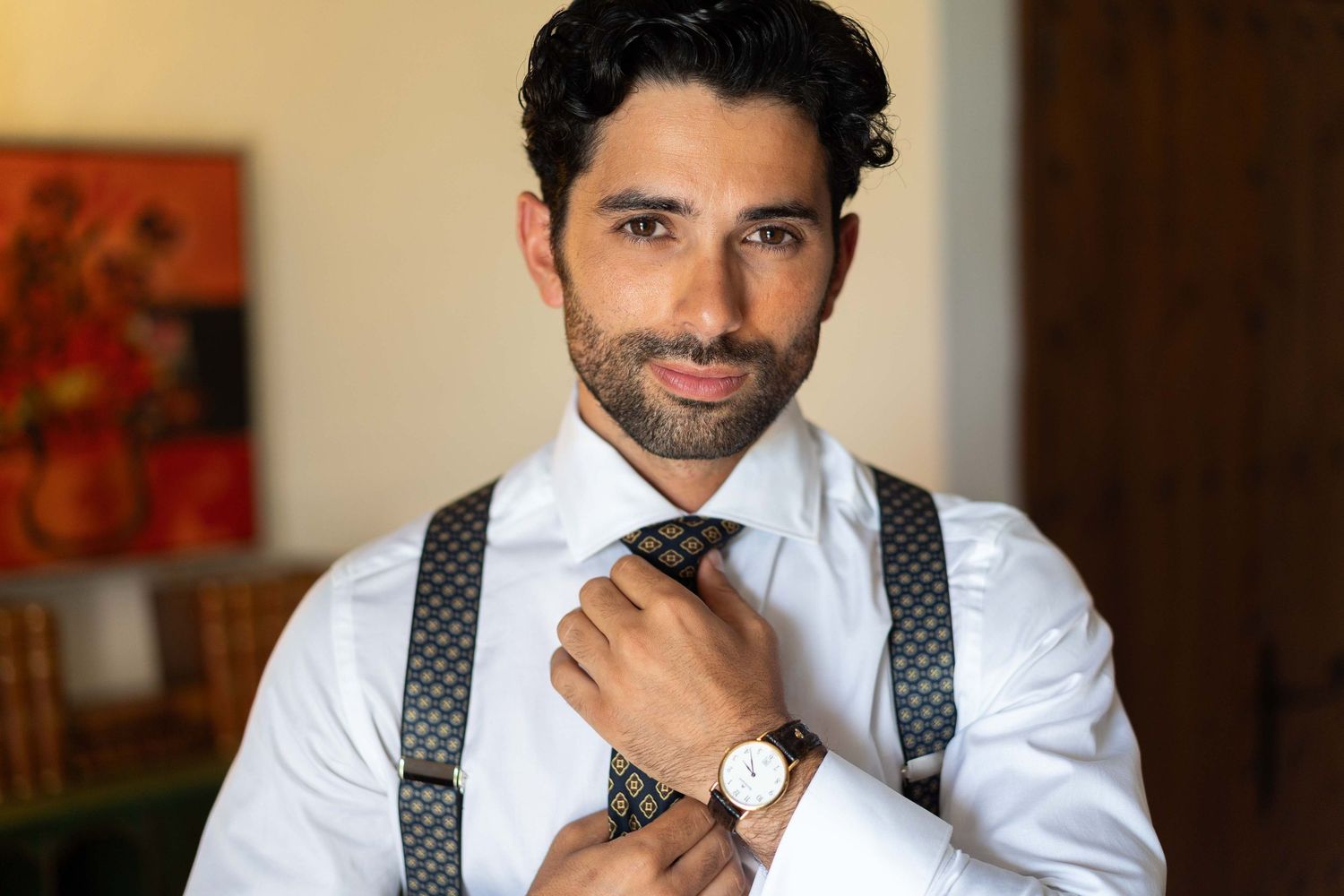 Groom getting ready in white shirt and polka dot suspenders.