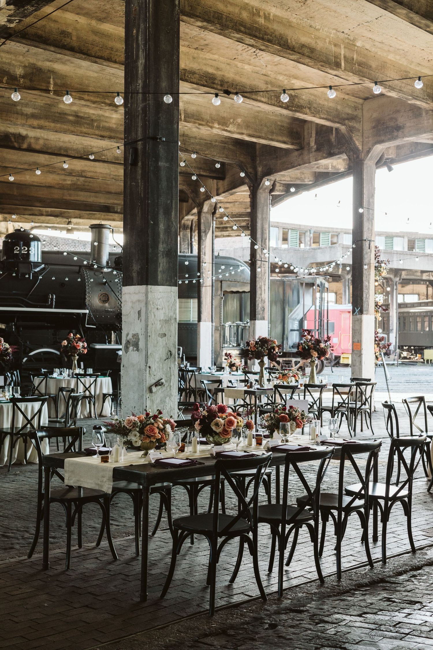 Industrial loft wedding reception venue with rustic wooden tables, string lights and exposed concrete beams.