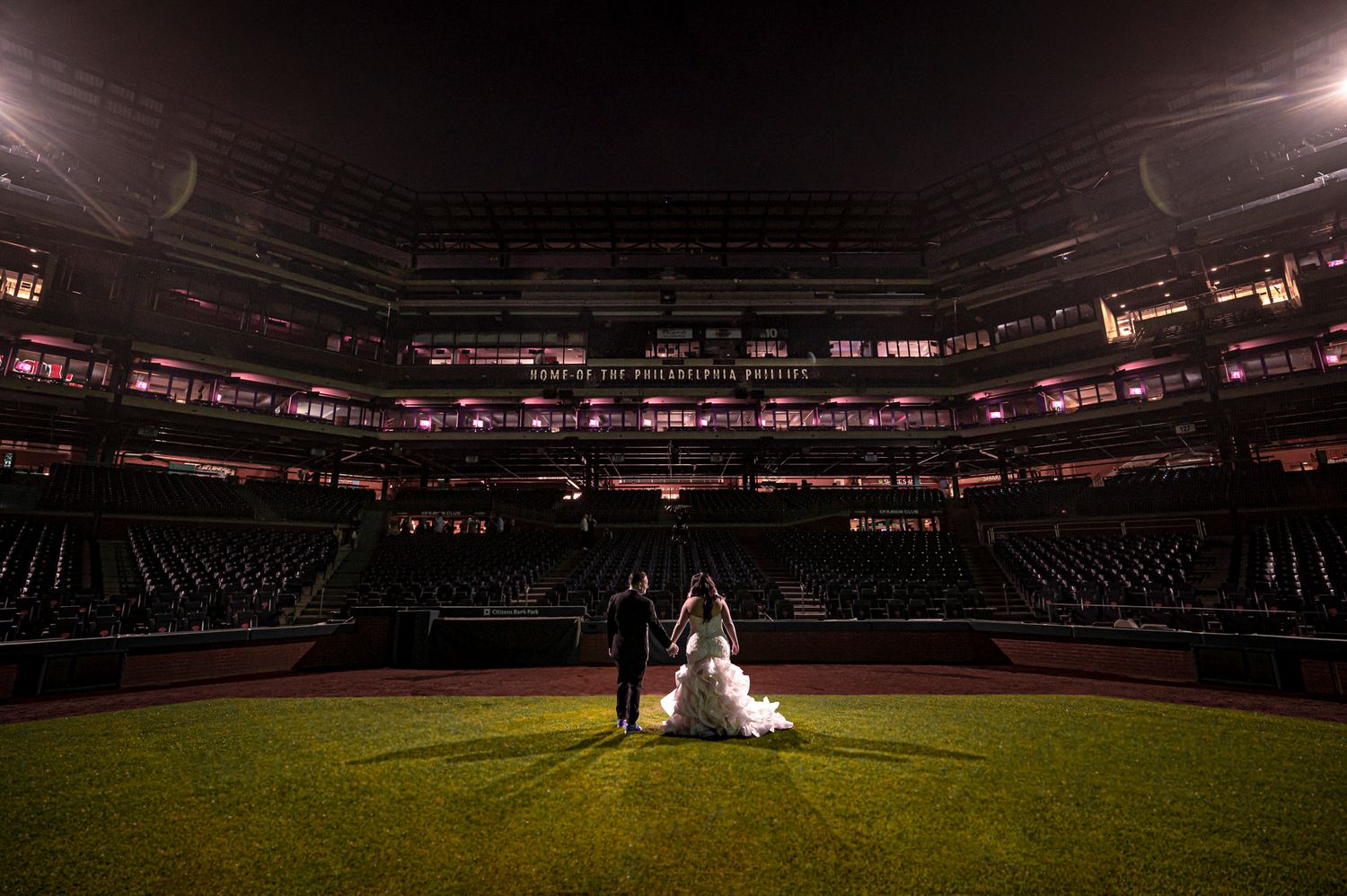 Baseball stadium panoramic view showing empty seats and field illuminated under bright stadium lights at night.
