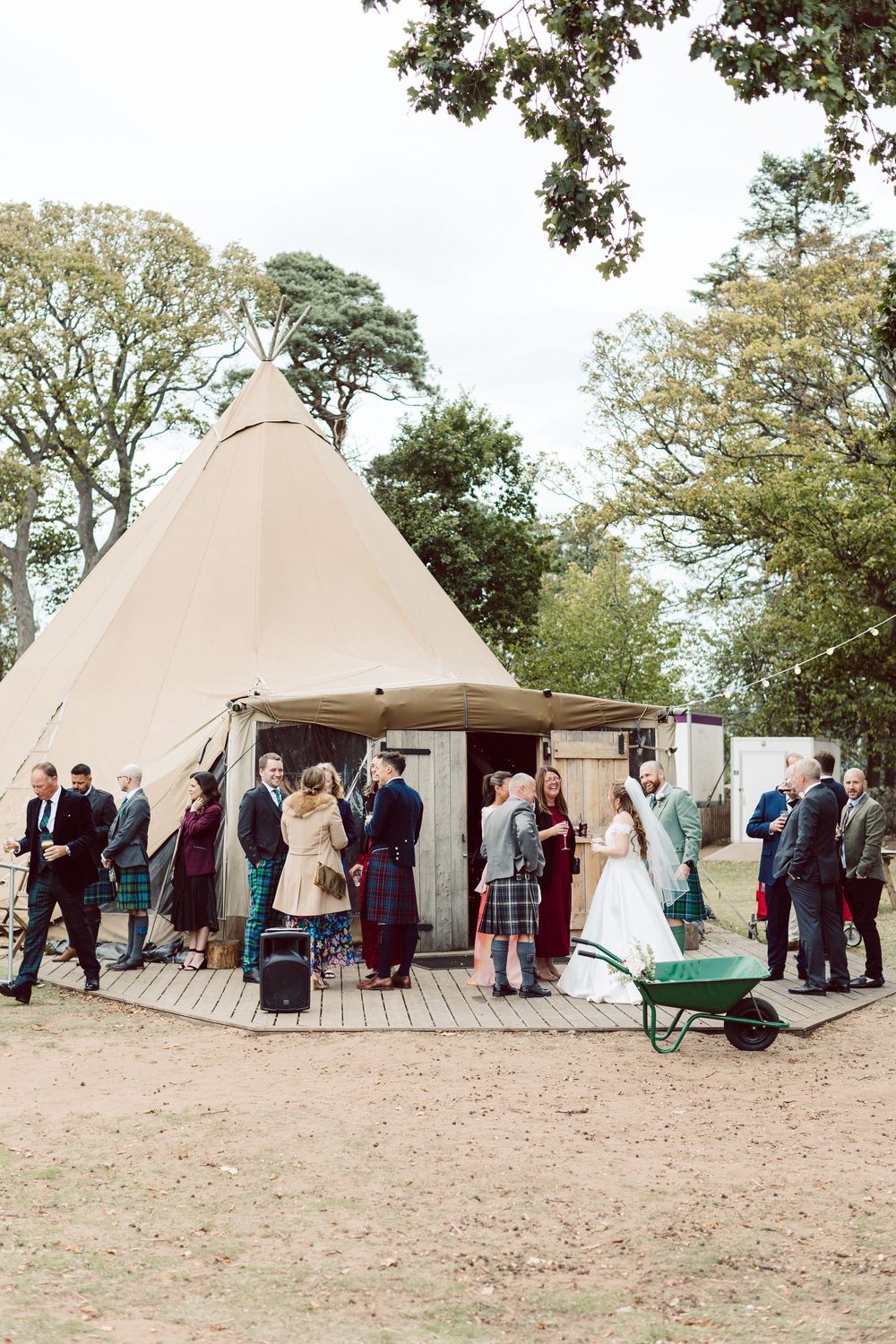 Wedding guests gather outside large beige teepee tents set up for an outdoor celebration.
