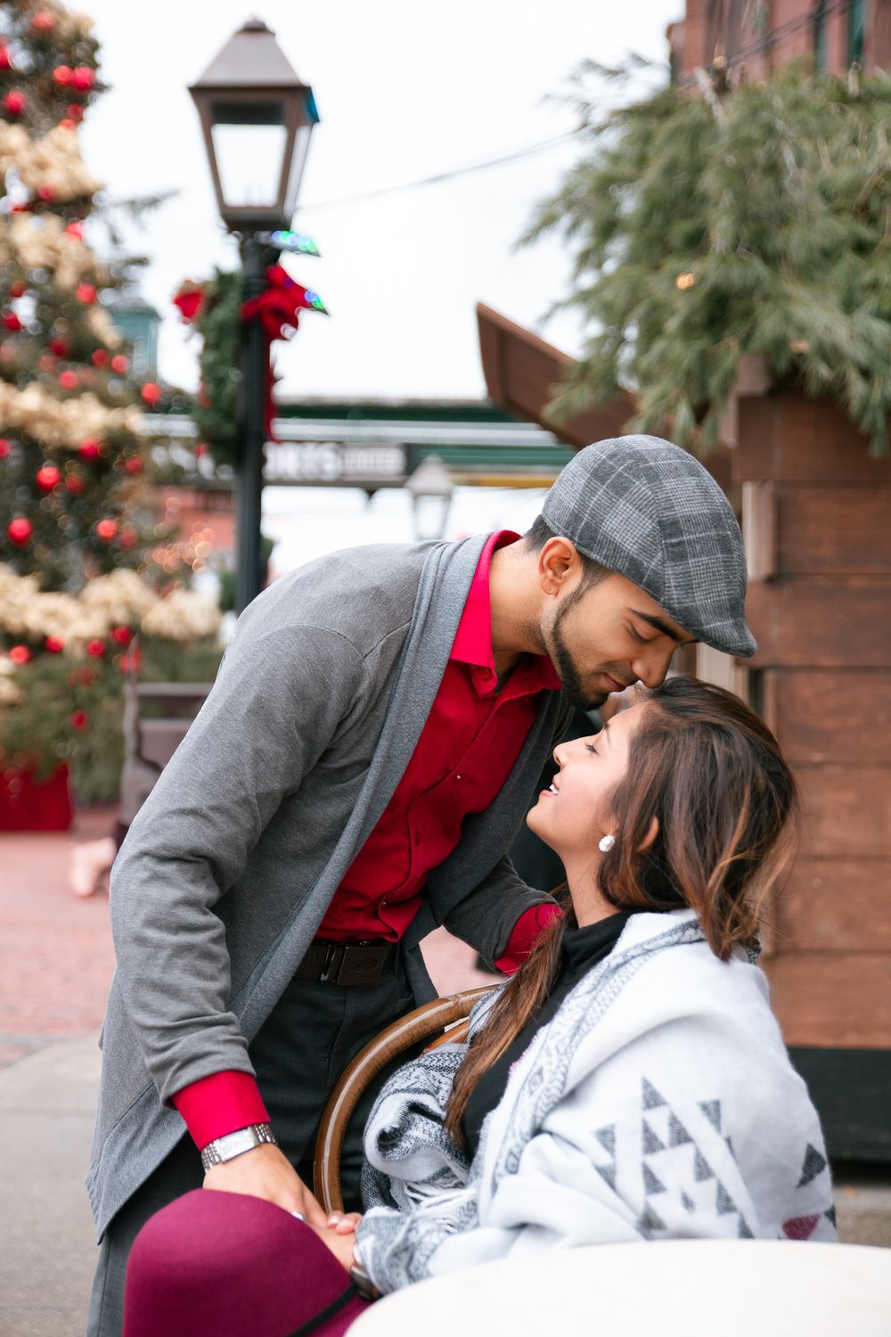 Romantic couple sharing a kiss near a decorated Christmas tree at holiday market.