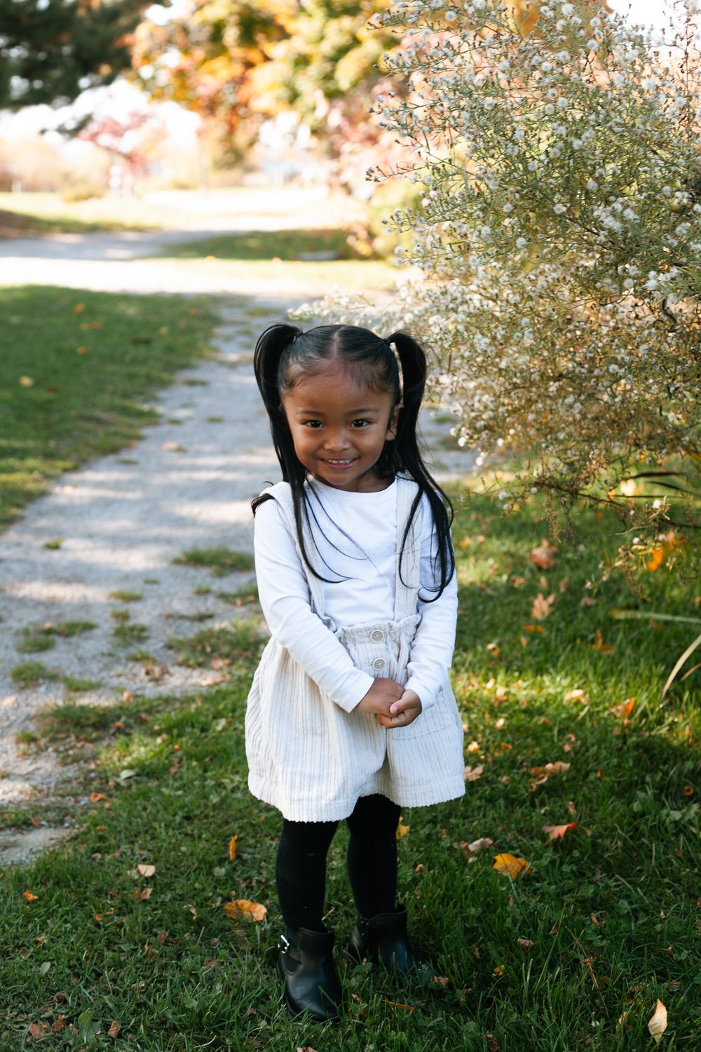 Adorable young girl in white dress with pigtails smiling outdoors in autumn park.