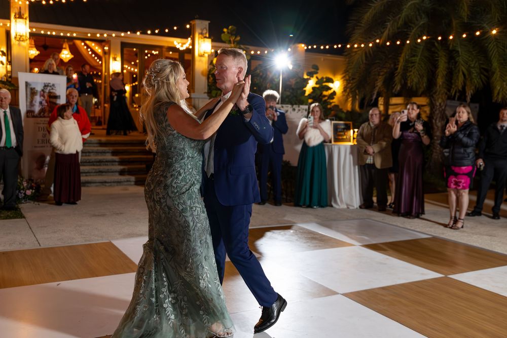 Couple dances on a white floor under string lights during an evening wedding reception.