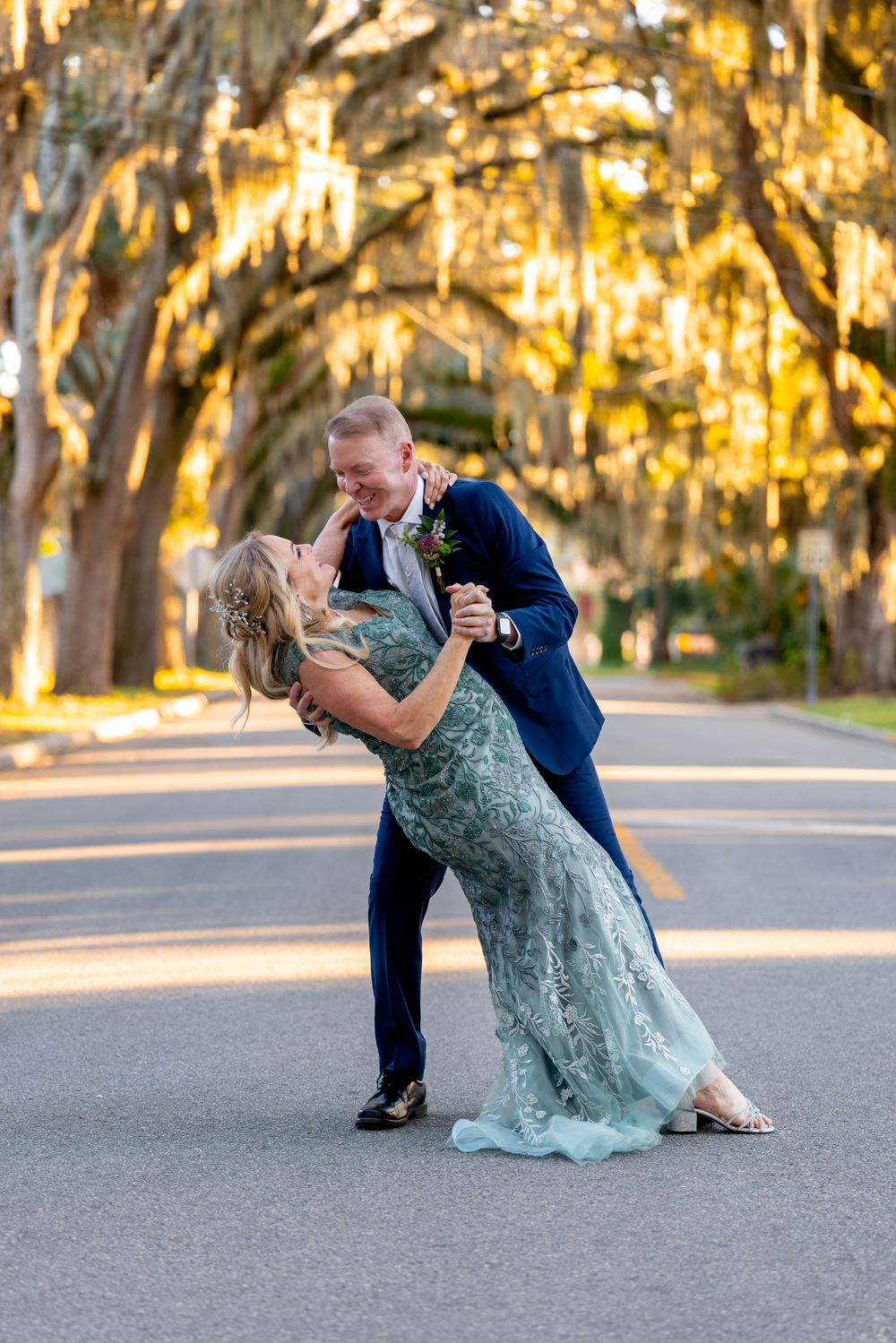 Romantic couple dances together in a dramatic dip pose on a road with Spanish moss draped trees at sunset.