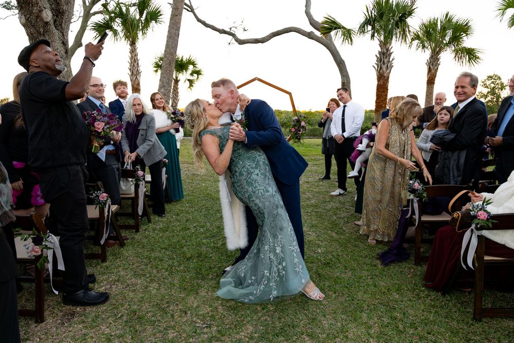 Wedding guests celebrate outdoors under palm trees during a daytime ceremony at a tropical venue.