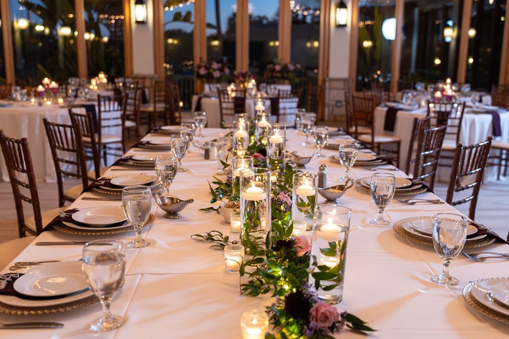 Elegant wedding reception tables set with white linens, floral centerpieces, and glowing candles in a grand ballroom setting.