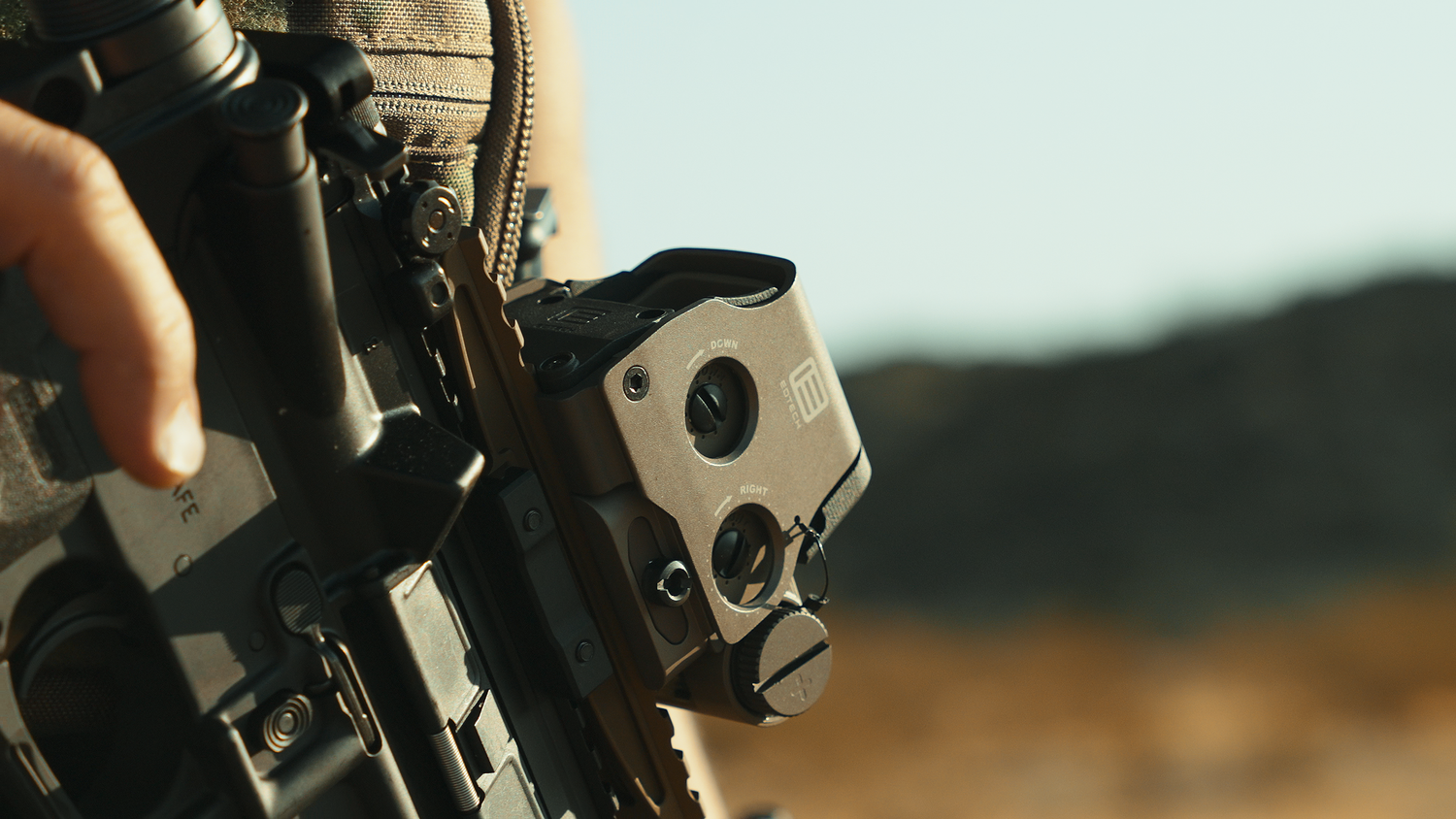 Tactical shooter practicing precision marksmanship with a rifle in desert terrain.