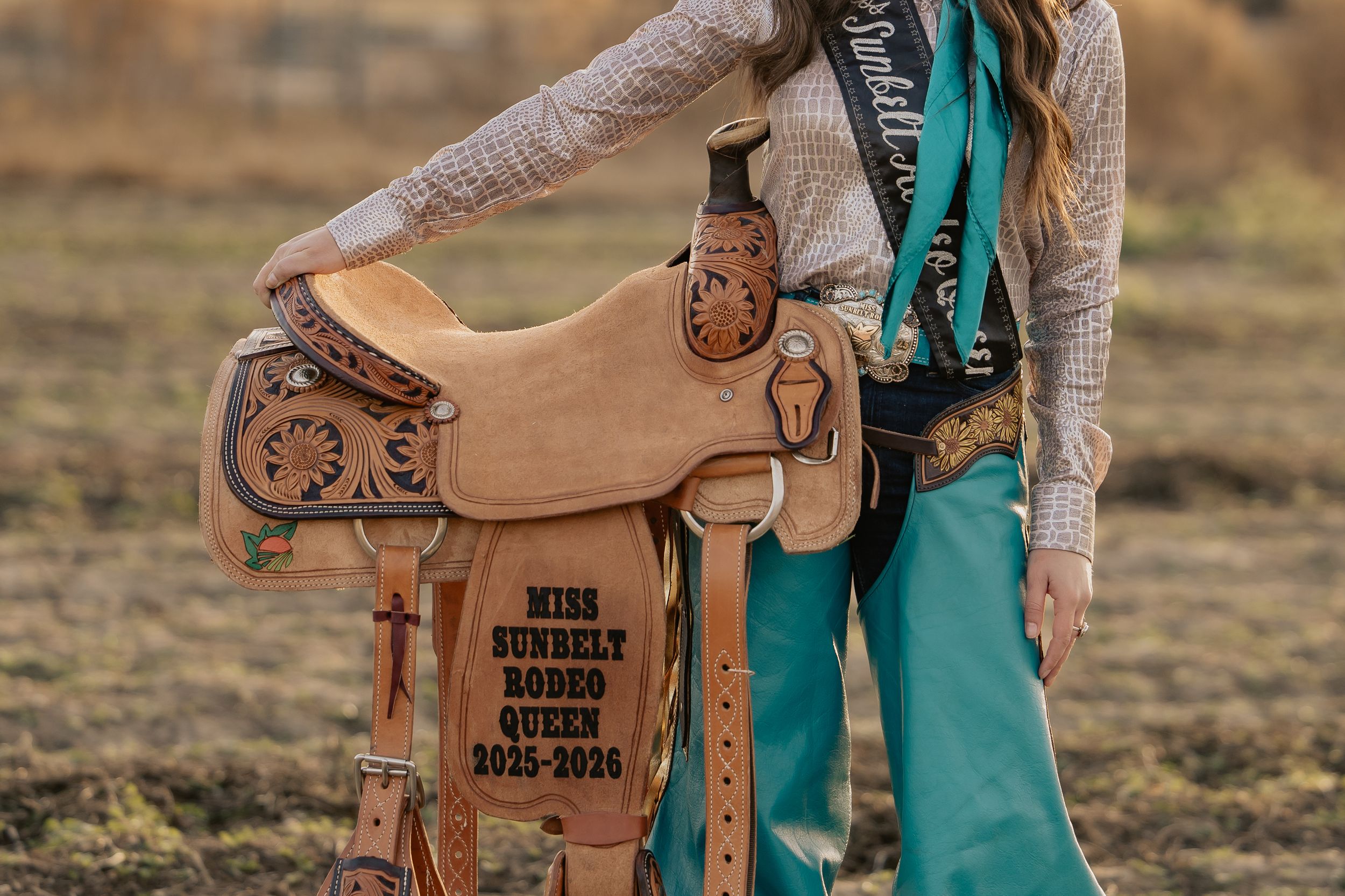 Miss Bundelt Rodeo Queen 2025-2026 posing with decorated western saddle in turquoise outfit.