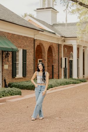Young woman in crop top and flared jeans posing in front of brick building with arched walkways.