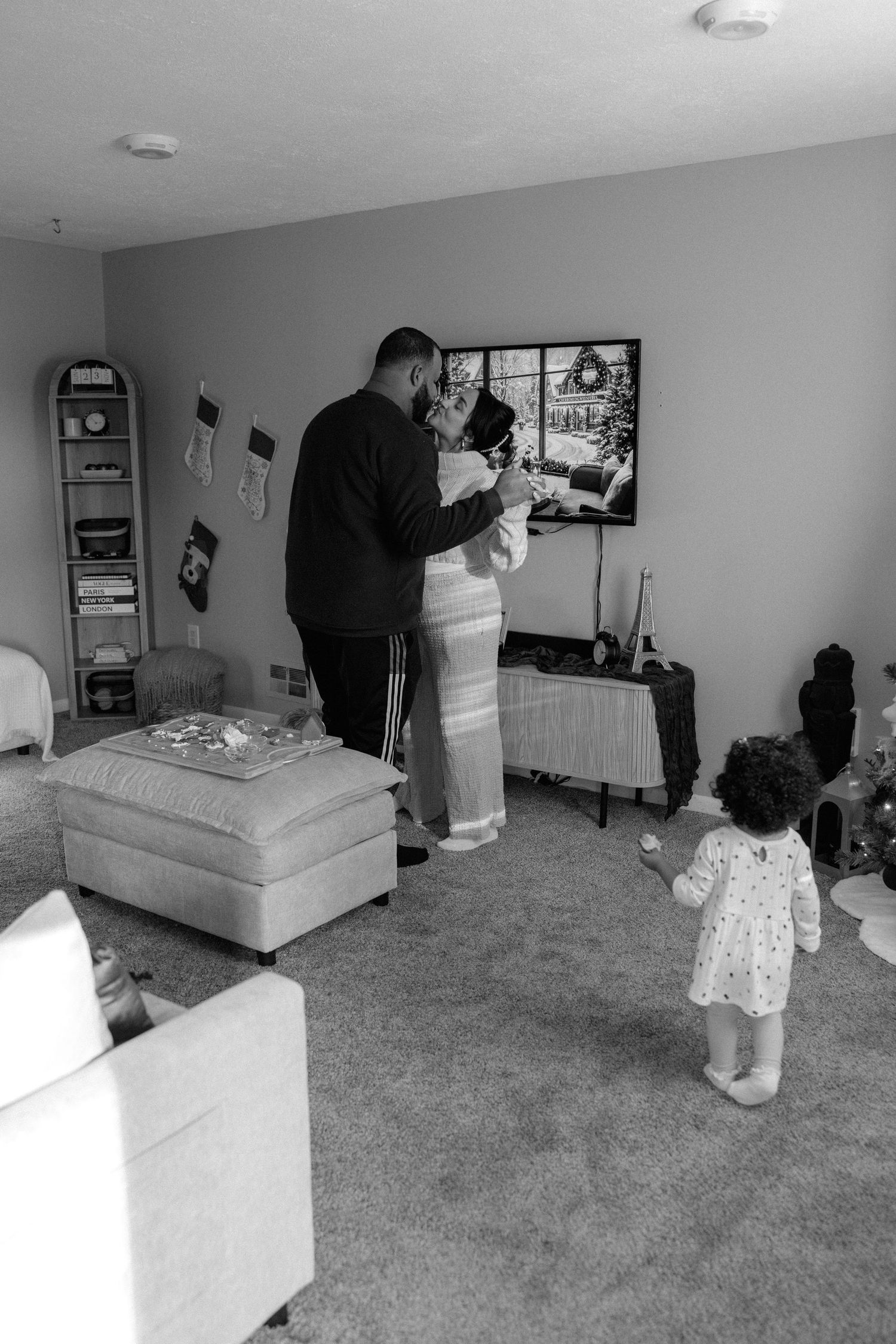 A series of black and white photos showing a child watching someone set up furniture in a carpeted room.