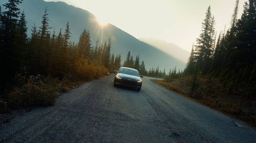 Car driving on winding mountain road through evergreen forest.