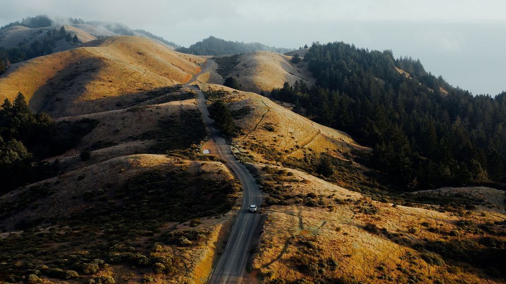 Rolling golden hills and mountain peaks with winding road cutting through landscape.