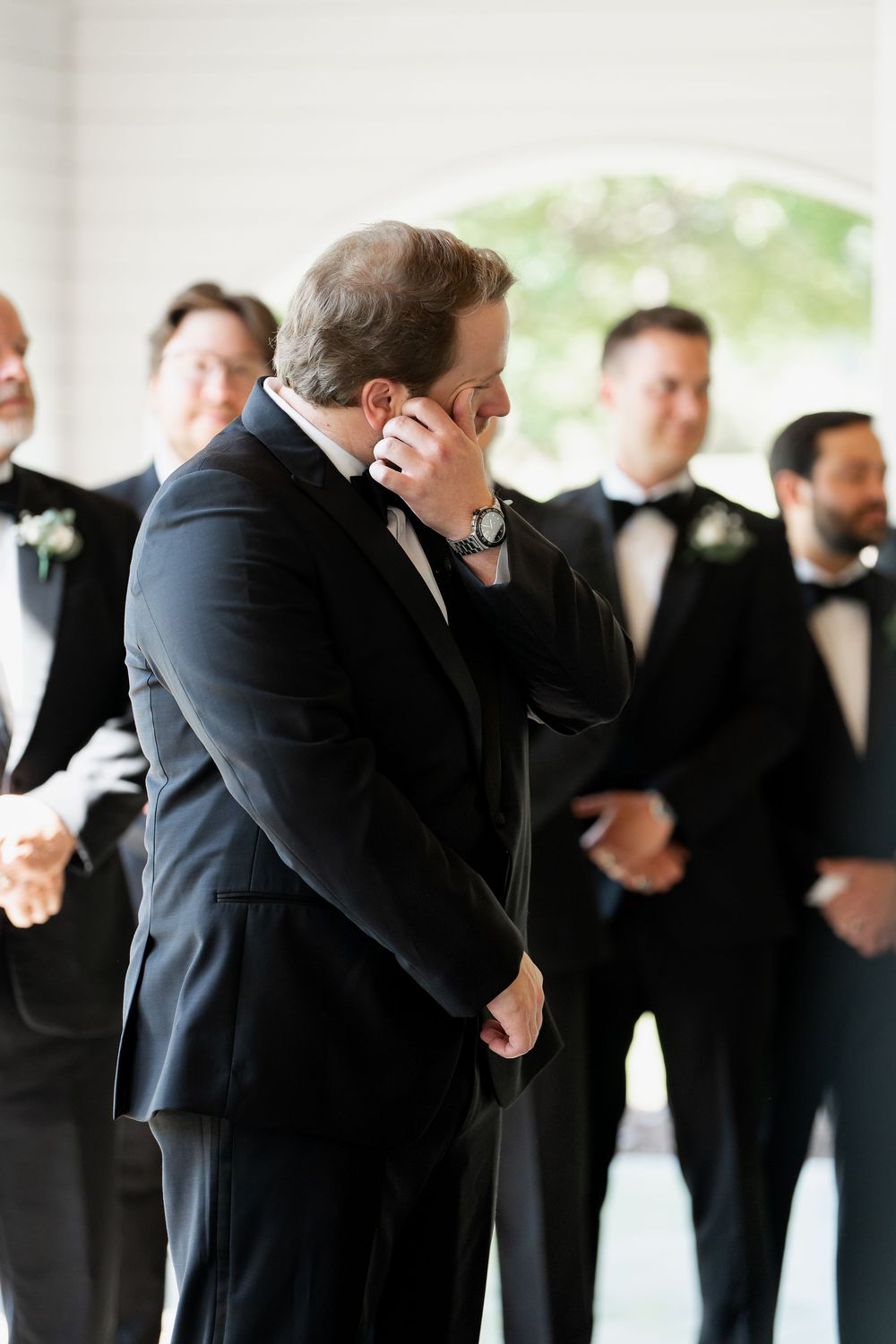 Groomsmen in black tuxedos share an emotional moment before the wedding ceremony.