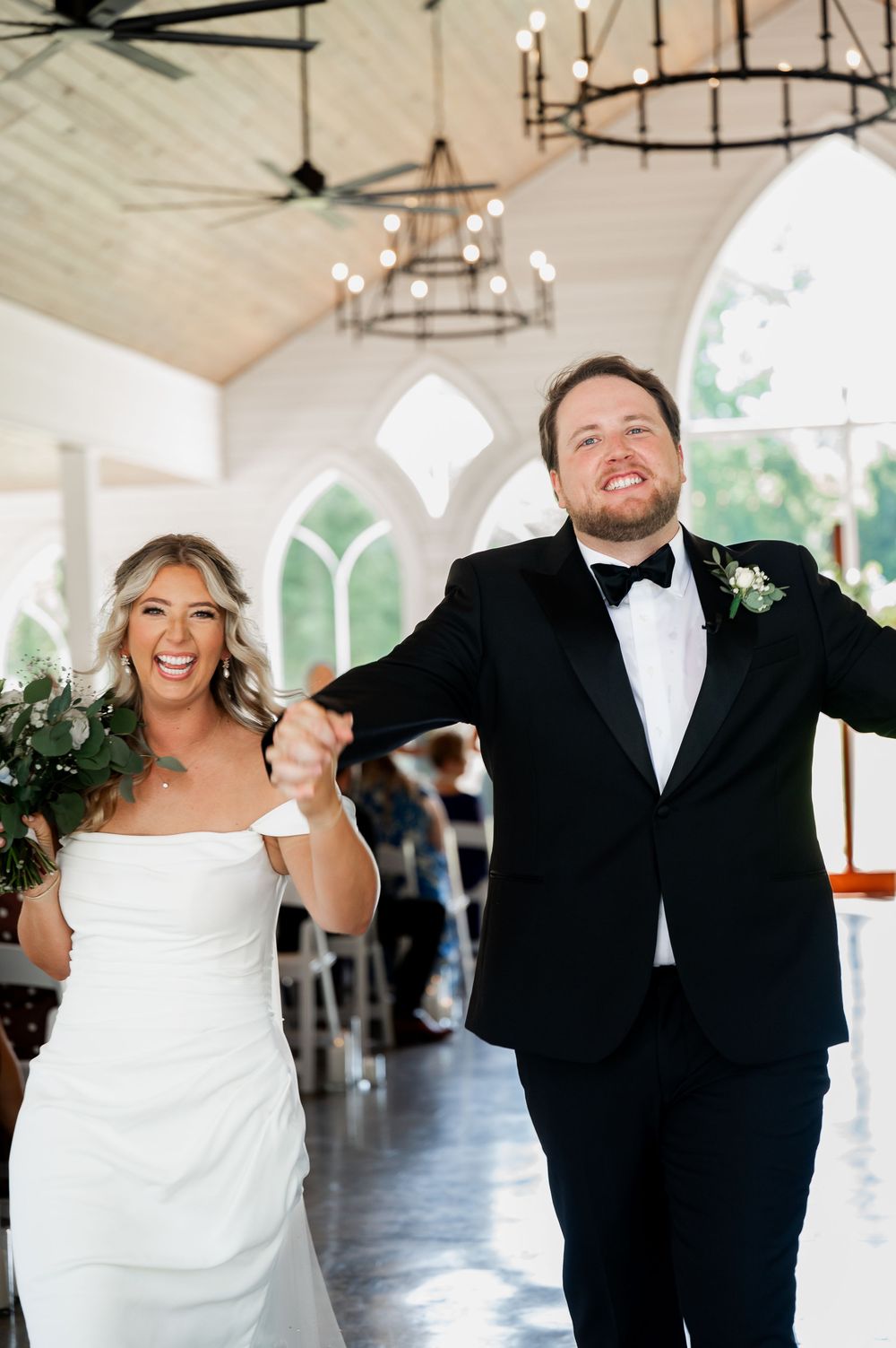 A joyful wedding couple dancing in a bright chapel with vaulted ceilings and elegant chandeliers.