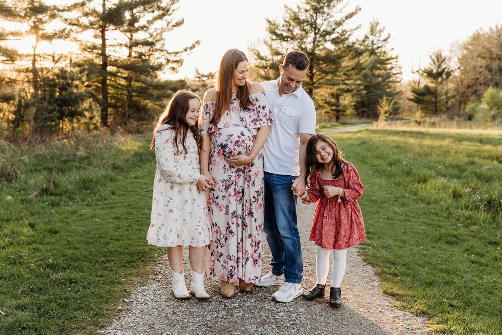 A family wearing coordinated red, white and blue outfits walks together on a grassy path at sunset.