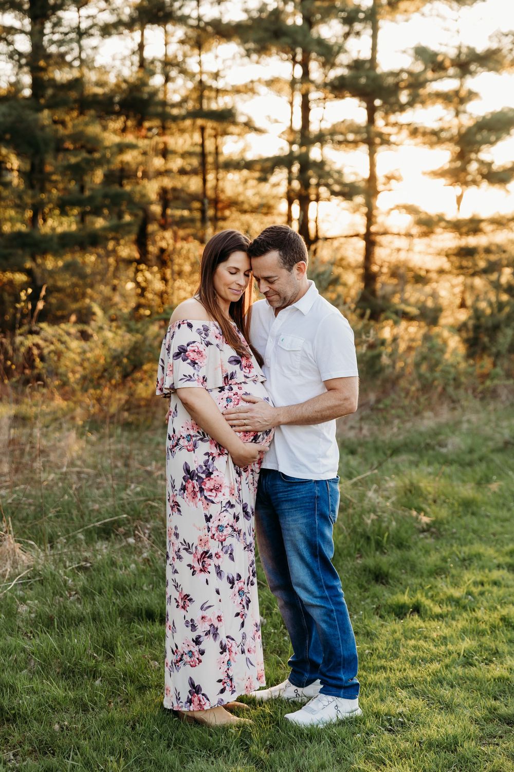 A couple shares an intimate moment in a sunlit meadow with pine trees during golden hour.