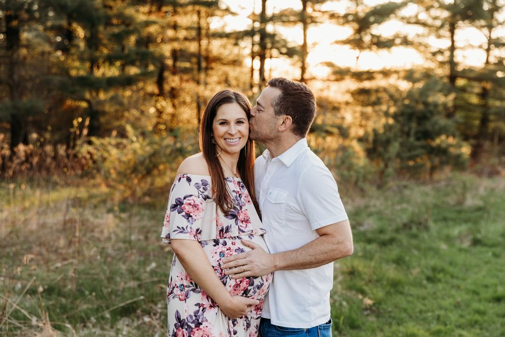 Romantic couple embraces in a sunlit meadow during golden hour with pine trees in the background.