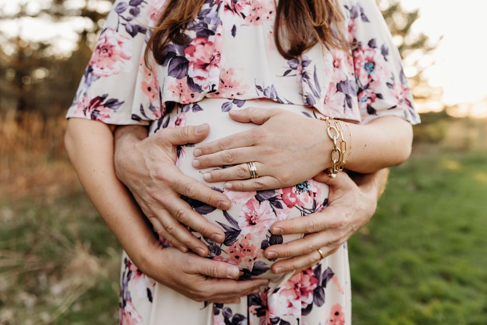 A person wearing a pink floral dress cradles their pregnant belly in a series of outdoor maternity photos at sunset.