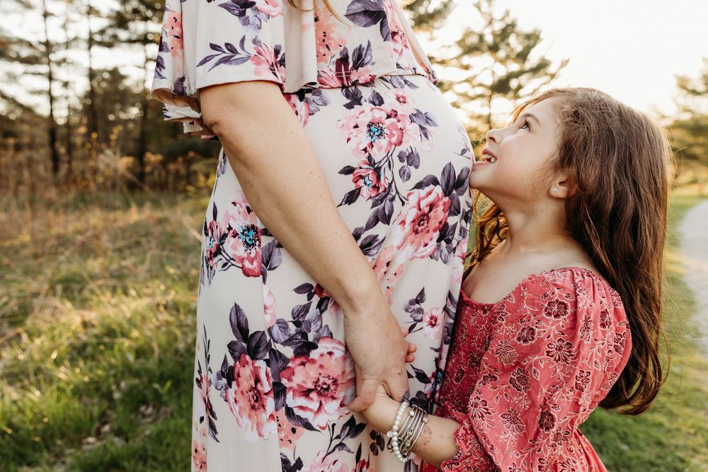 A tender moment shared between mother and child in floral dresses against a sunlit outdoor backdrop.