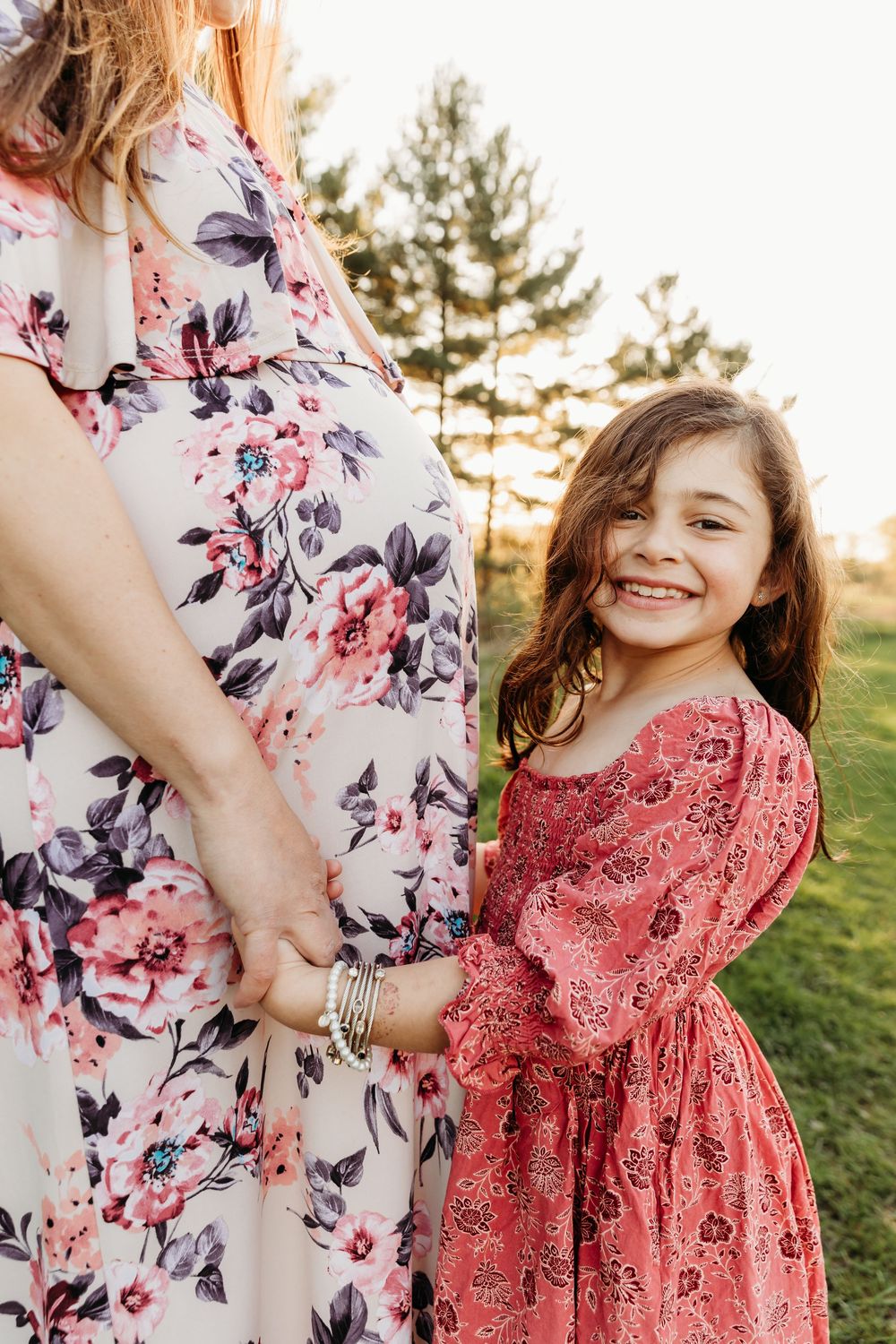 A sweet moment captured at sunset showing coordinated floral and coral outfits in a grassy outdoor setting.