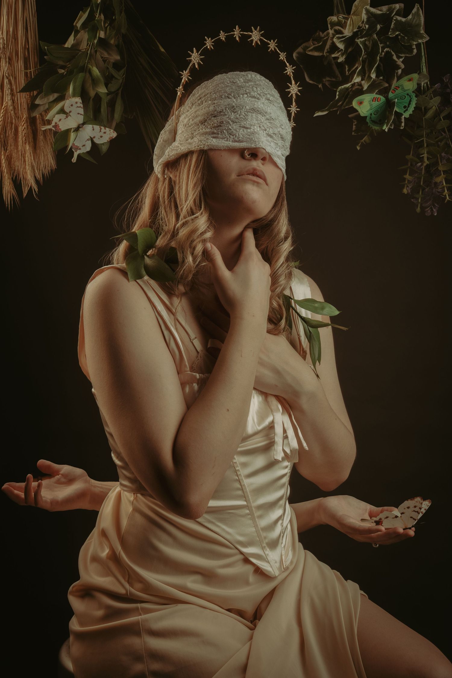 Artistic portrait in silk dress with dramatic lighting and floral elements in dark moody setting.