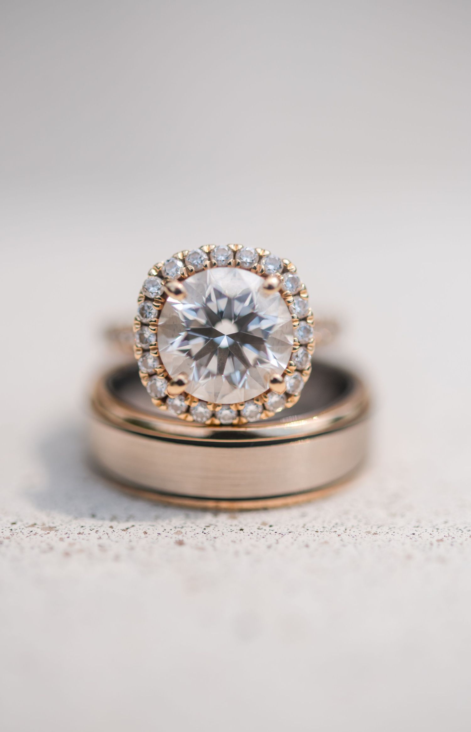 Close-up view of a rose gold engagement ring with a round diamond center stone and delicate halo setting on a textured surface.