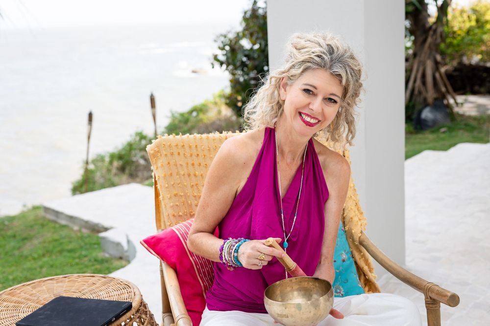 Someone in a bright magenta top sits in a wicker chair outdoors while holding a singing bowl.