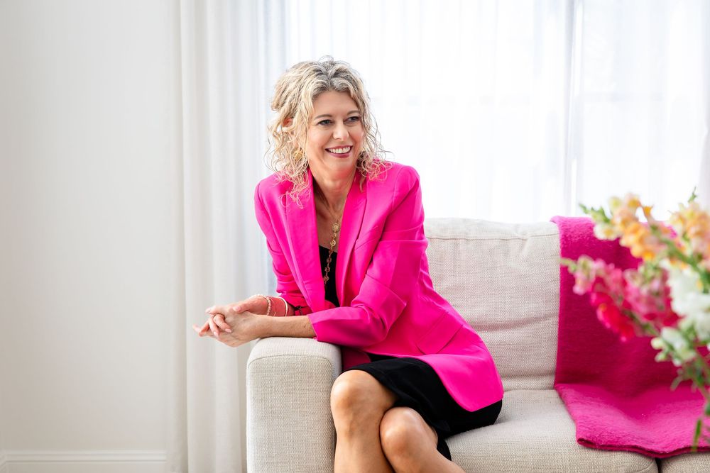 Professional lifestyle photoshoot featuring someone in a vibrant hot pink blazer sitting by a bright window.