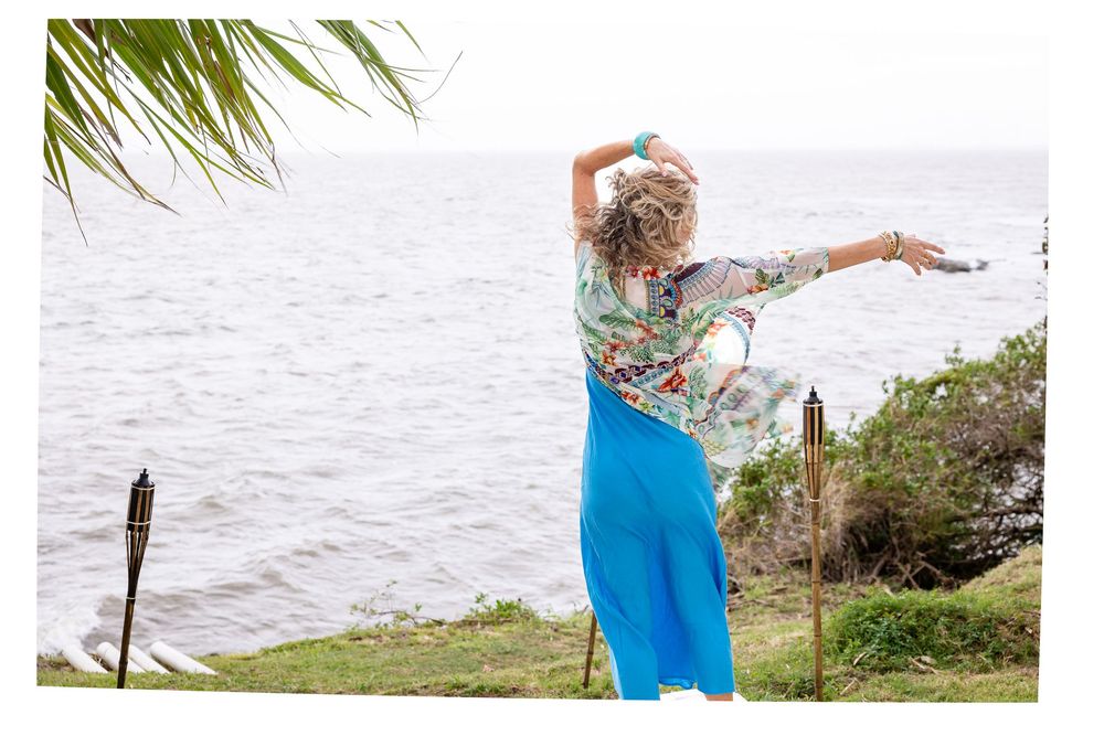 Person in blue outfit standing by palm trees near waterfront on sunny day.