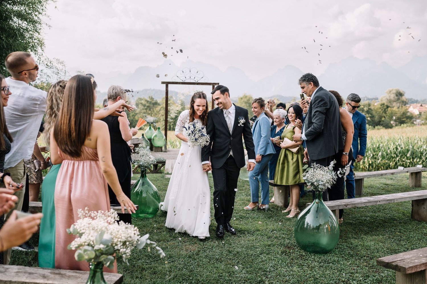 Gli invitati al matrimonio si riuniscono all'aperto su una collina erbosa durante una celebrazione in un pomeriggio soleggiato.