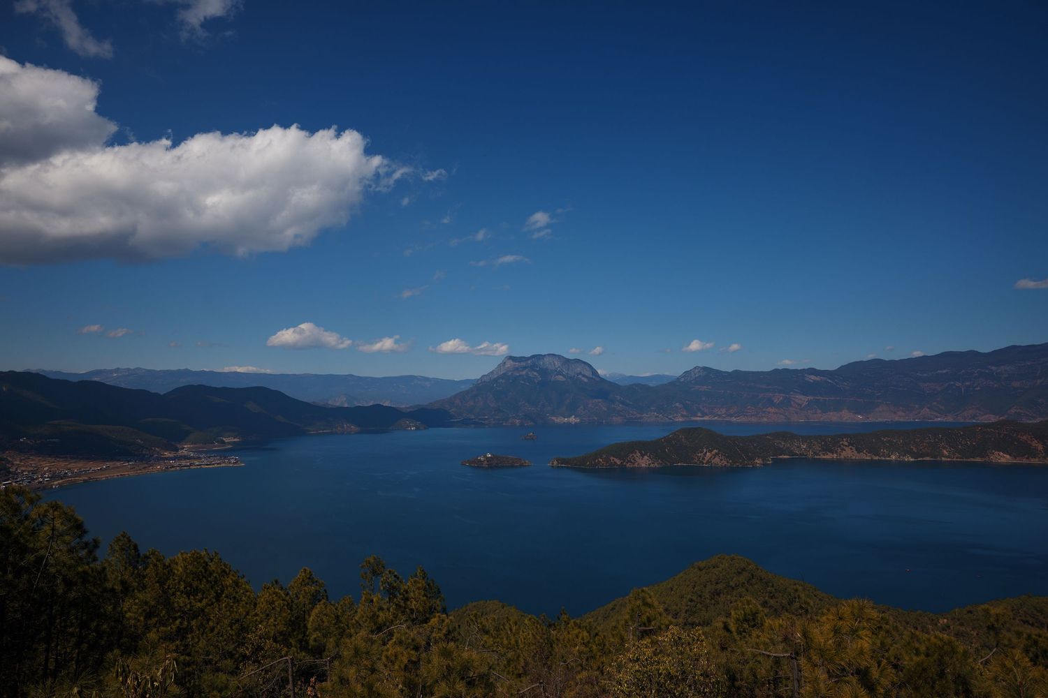 Scenic aerial view of Lake Lugu in Yunnan China with blue waters surrounded by mountains under a partly cloudy sky.