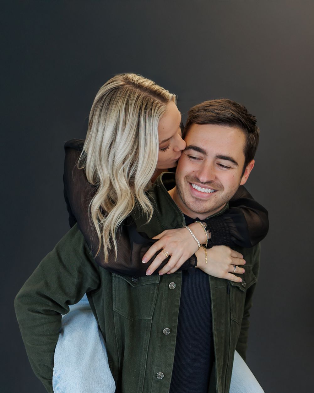 A couple shares an intimate moment in a photo series showing affection and laughter against a dark background.