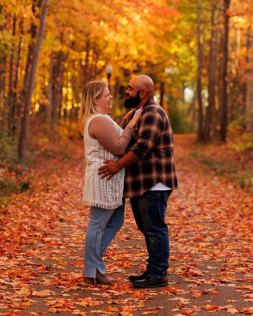 A couple embraces in a romantic autumn setting surrounded by vibrant orange and yellow fallen leaves in the forest.