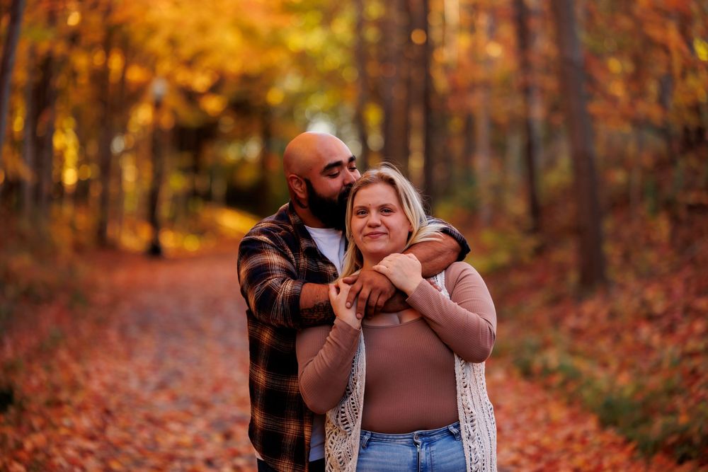 Couple embracing in autumn forest surrounded by vibrant orange and red fall foliage during sunset.