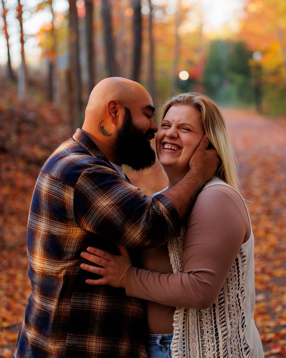 A couple shares a tender moment together on a path covered in autumn leaves during golden hour.