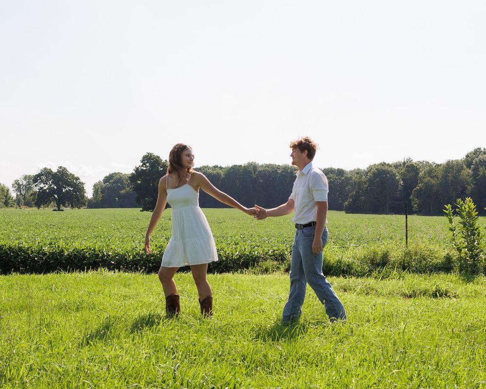 A couple walks hand in hand through a sunny meadow on a summer afternoon.