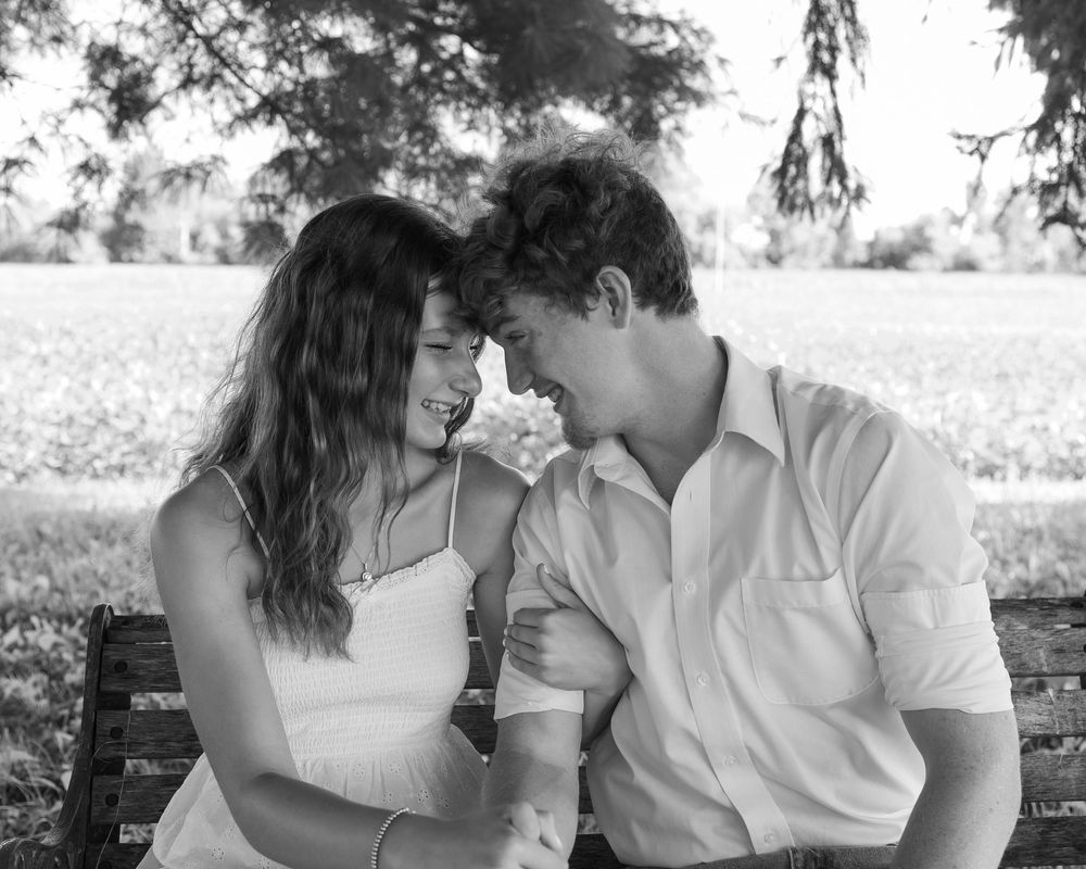 A romantic couple shares tender moments in a black and white photo series outdoors under trees.