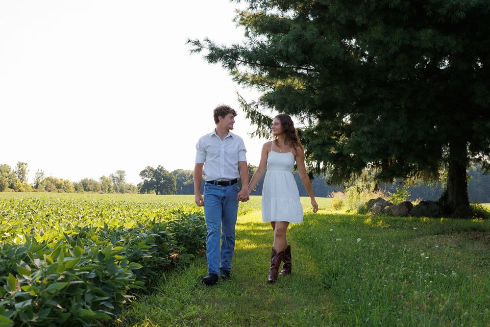 People stroll together along a grassy path bordered by lush trees and greenery.