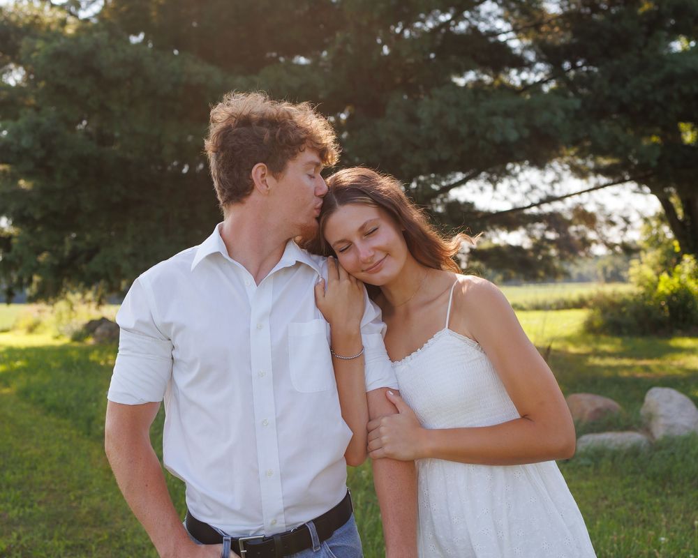 A romantic couple in white outfits shares tender moments together in a sunlit outdoor garden setting.