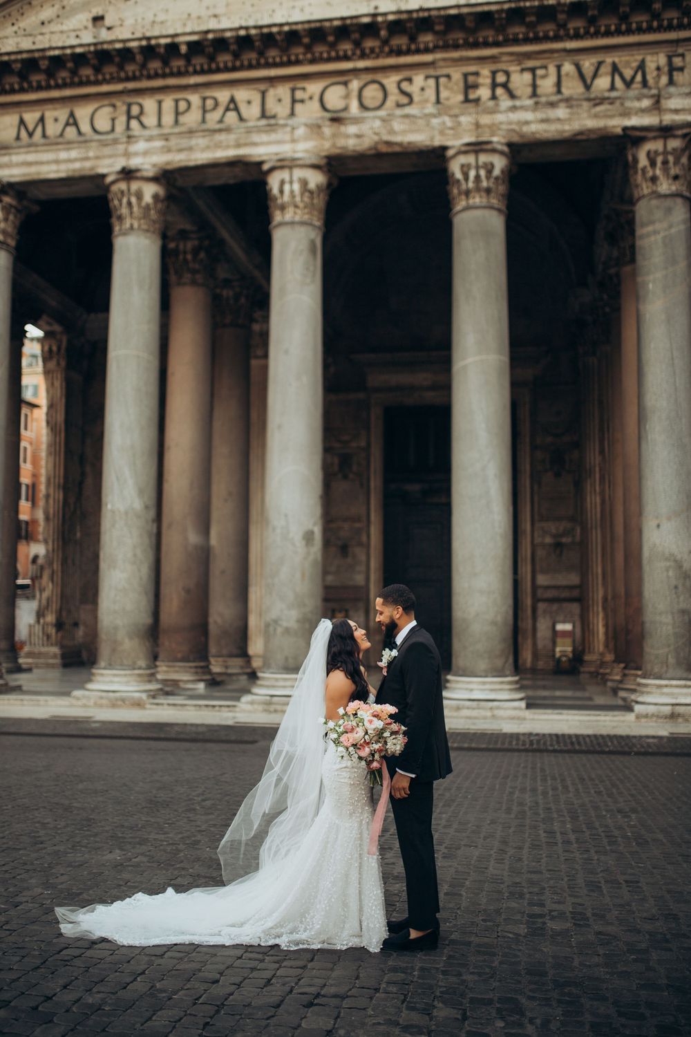 Elegant wedding couple embraces in front of historic Pantheon building with grand Roman columns in Rome, Italy.