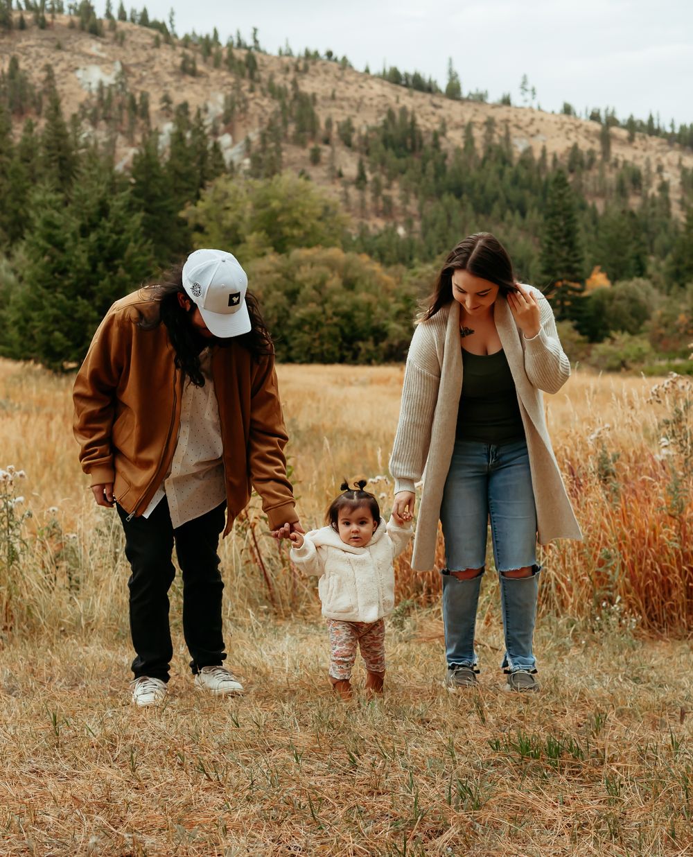 Family walking together through a scenic mountain meadow during fall with golden grass and evergreen trees.